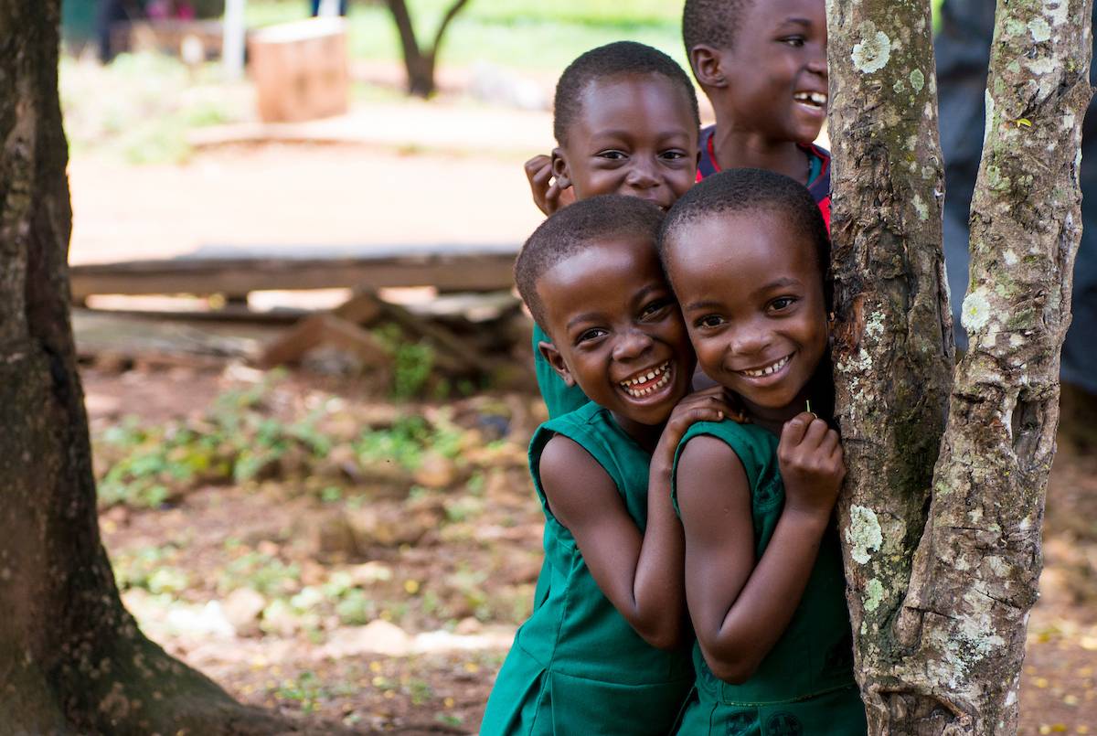 Three little girls from Ghana hugging and smiling next to a tree.